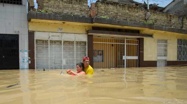 Un hombre ayuda a una mujer a cruzar una calle inundada por el río Piura
